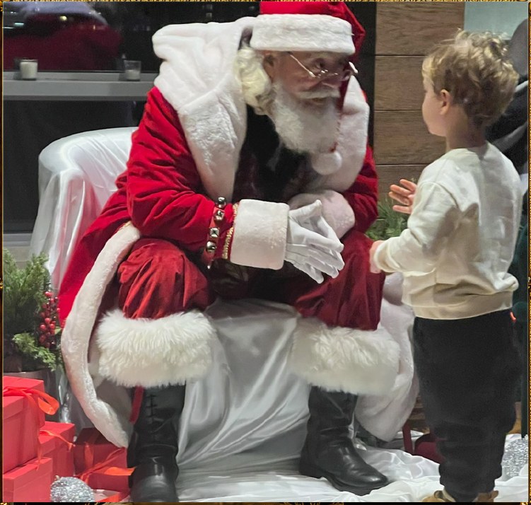 Santa James leaning forward and listening closely to a young boy.