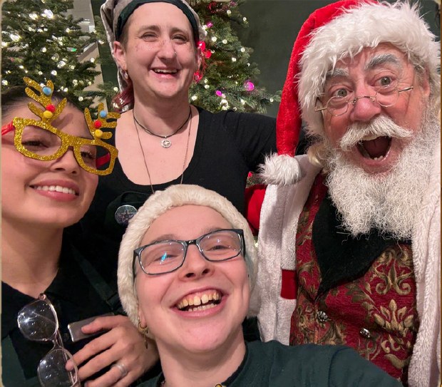 Santa James laughing in a group selfie with adults at a Christmas celebration.