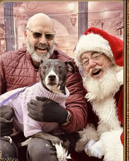 Santa James smiling beside a guest holding a dog.